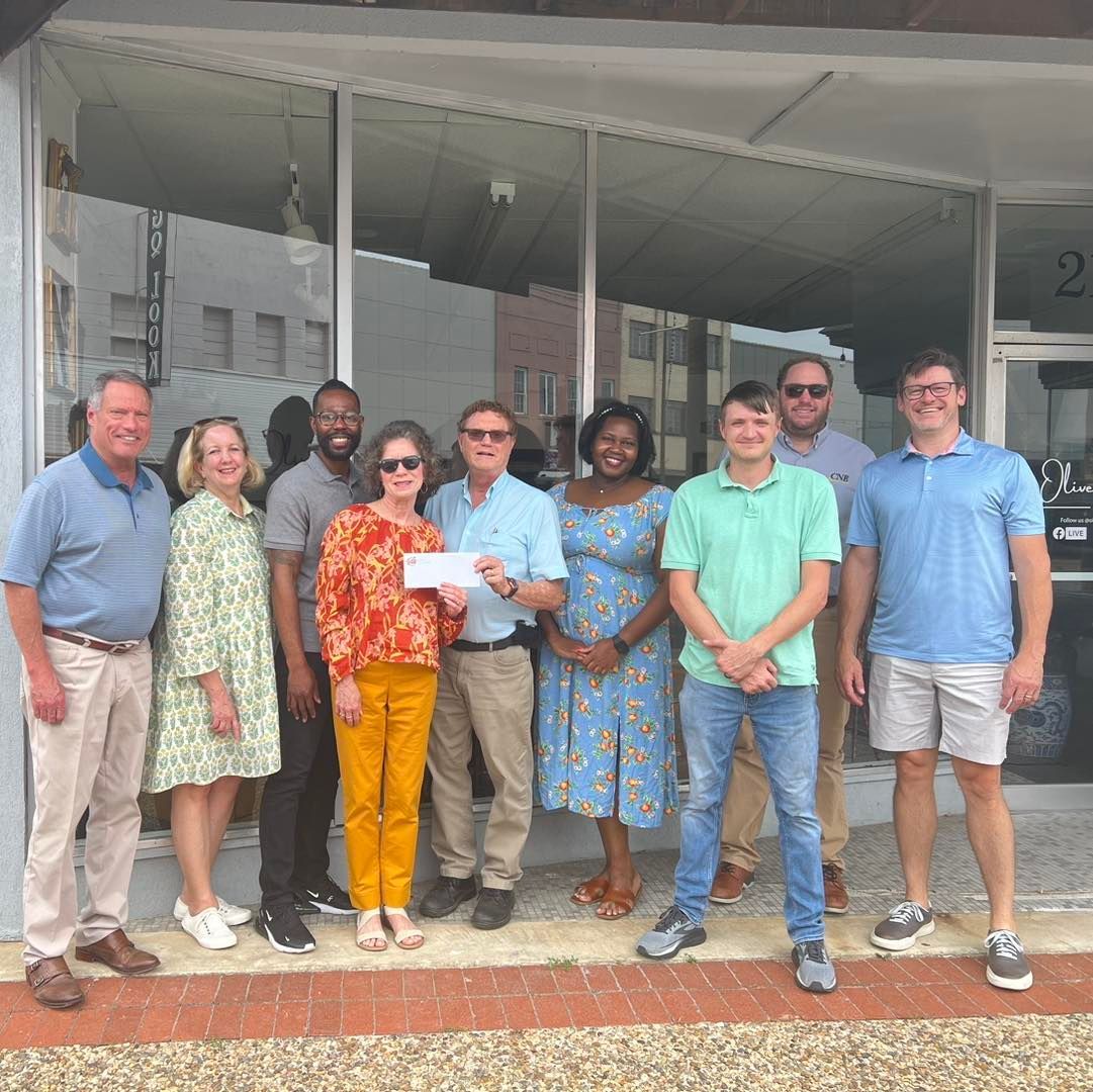 Group of people holding a check in front of a store with glass windows.
