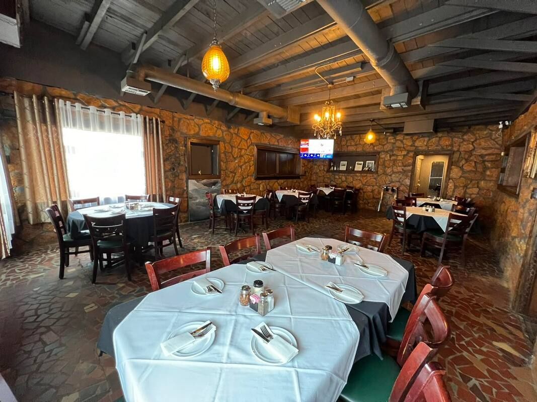 Restaurant dining room with stone walls, tables set with white tablecloths, and a large window.
