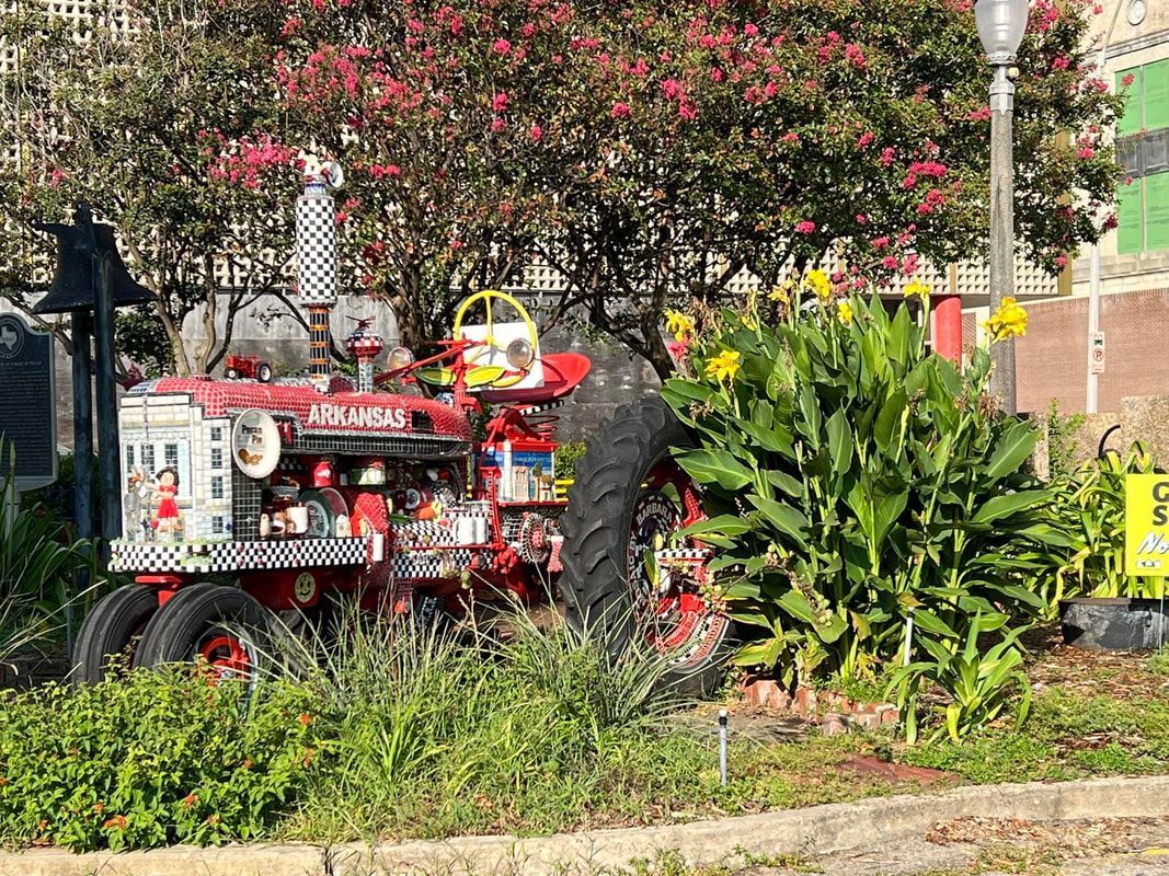Decorated red tractor with checkered accents, parked near flowers and shrubbery.