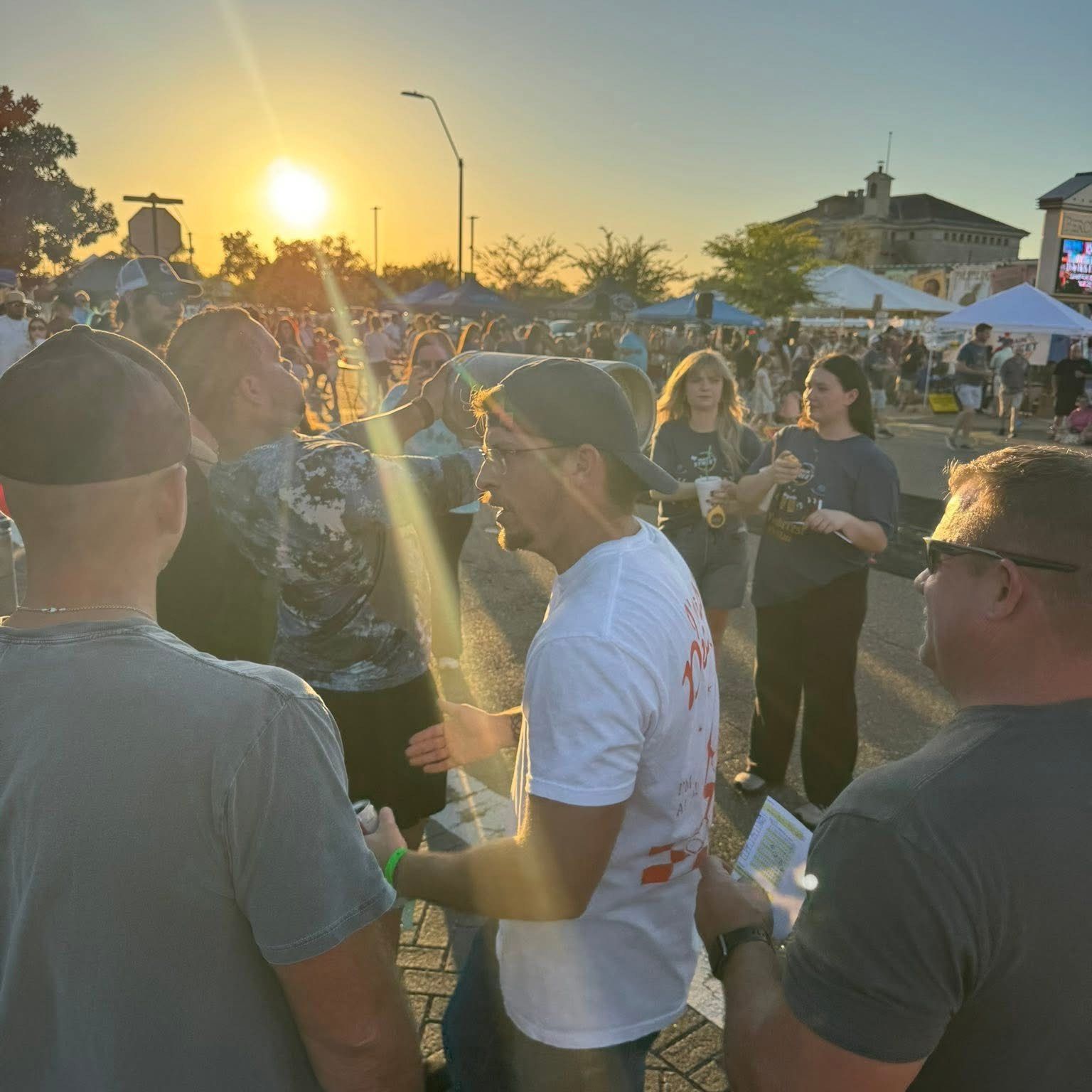 People gather outdoors at sunset, illuminated by the bright sun.