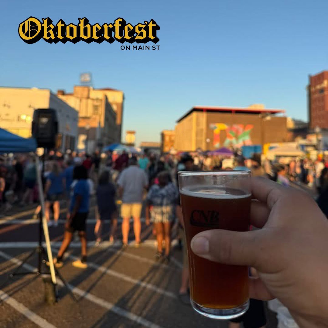 Hand holding a beer at Oktoberfest in a crowded street. Buildings and people are in the background, bathed in sunlight.