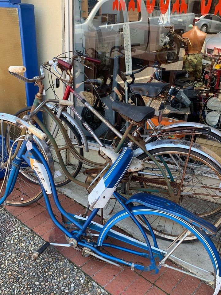 Several vintage bicycles in front of a shop window, mostly blue and rusty metal frames.