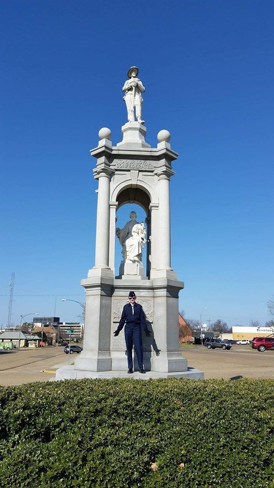 Person standing in front of a tall, ornate stone statue under a clear blue sky.