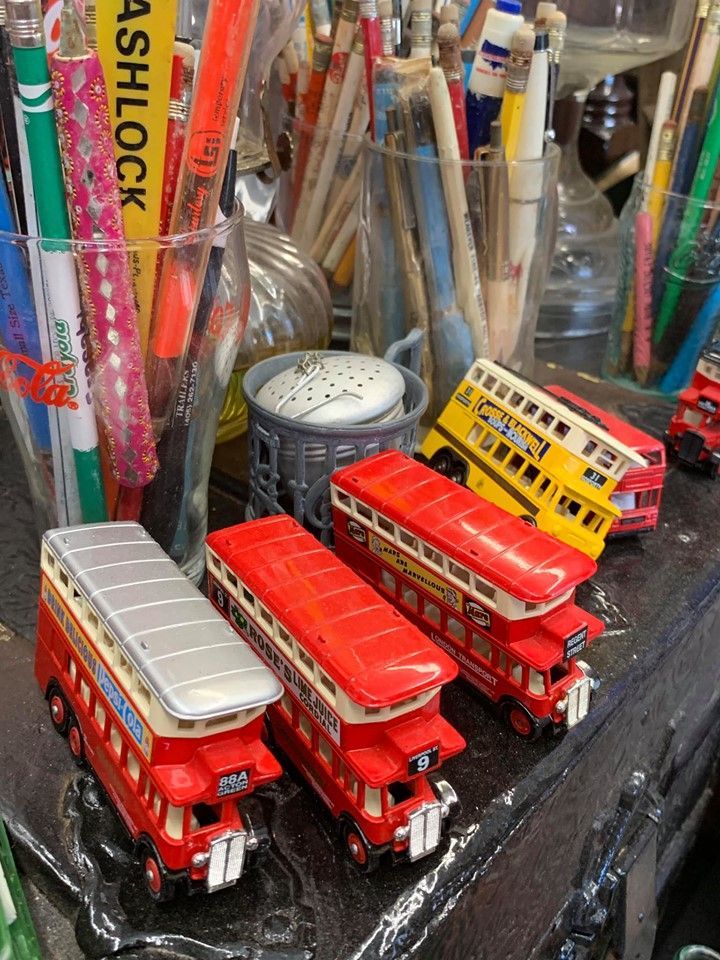 Toy double-decker buses, mostly red, sit near pens and pencils in clear containers.