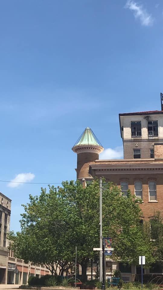 Brick buildings and a tower with a green roof against a blue sky, street view.