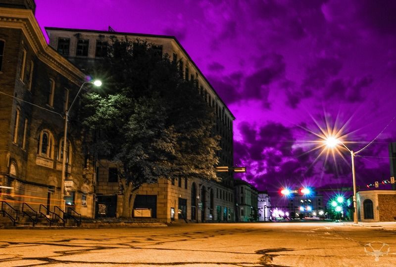 Street view at night with buildings, illuminated streetlights, and a vibrant purple sky.