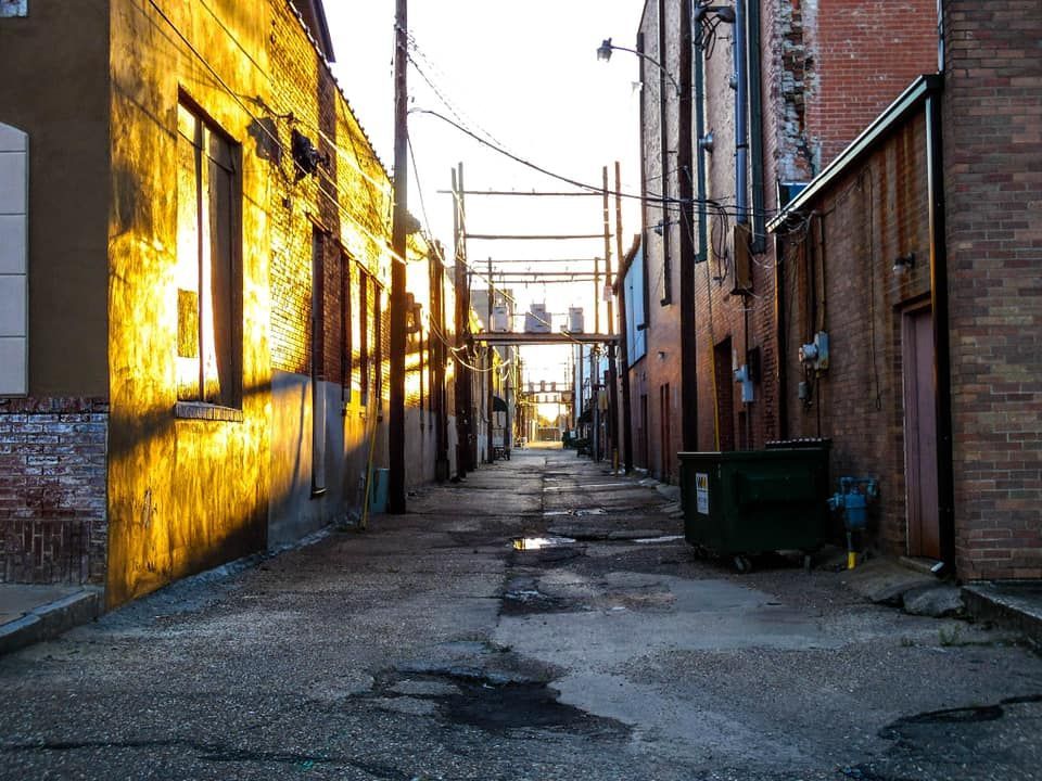  Cobblestone street leads to distant city skyline, power lines overhead, dumpster on right.