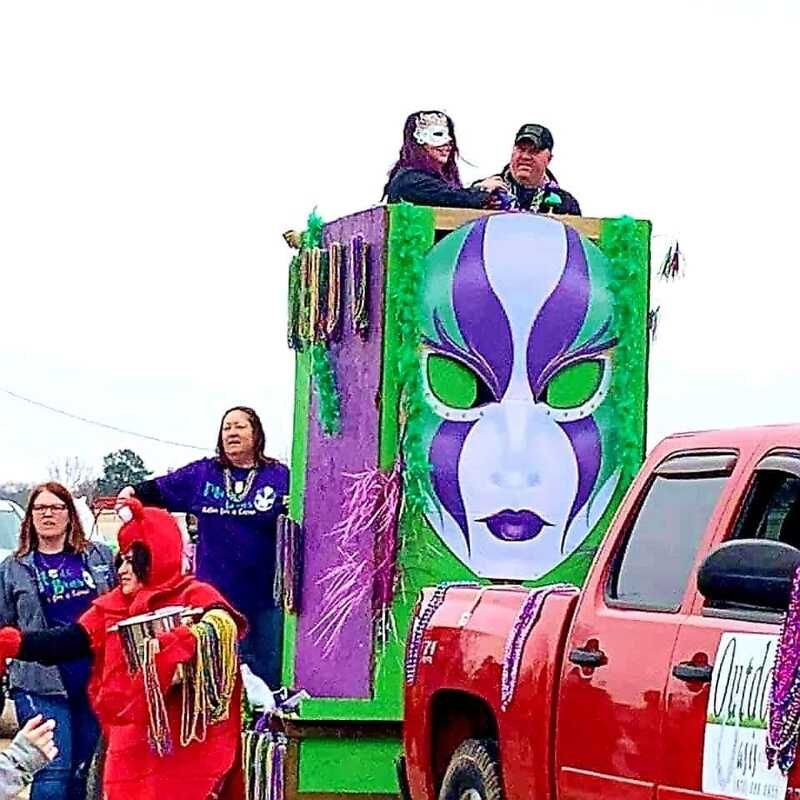 Mardi Gras float with a mask on it, red truck, people in costumes and throwing beads.