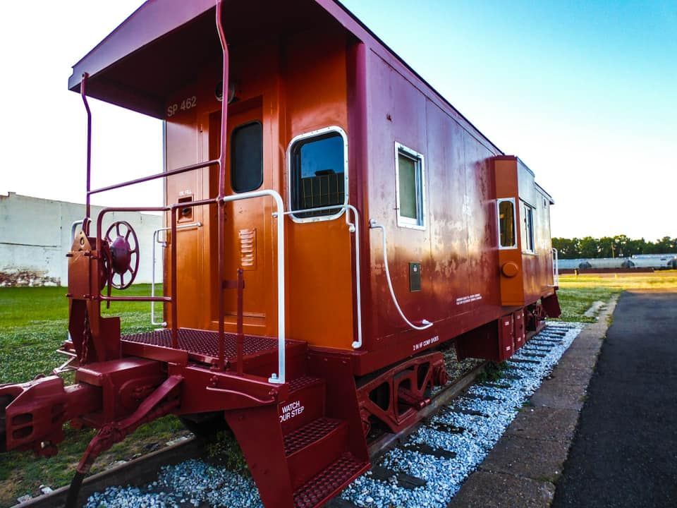 Red caboose on tracks, with steps and windows, set outdoors.