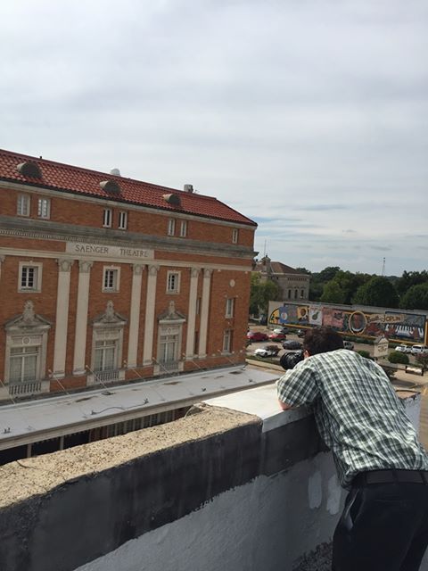 Man leaning on a rooftop, looking at the Orpheum Theatre with its red tile roof and ornate facade, cloudy sky.