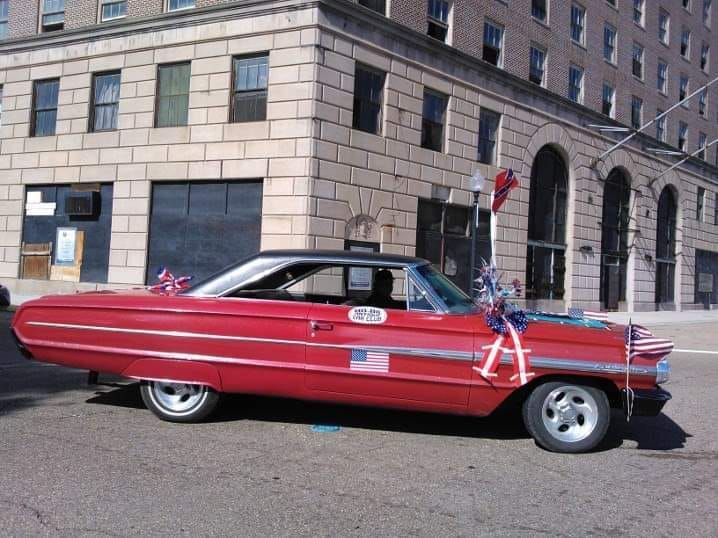 Red classic car decorated with flags parked in front of a brick building.