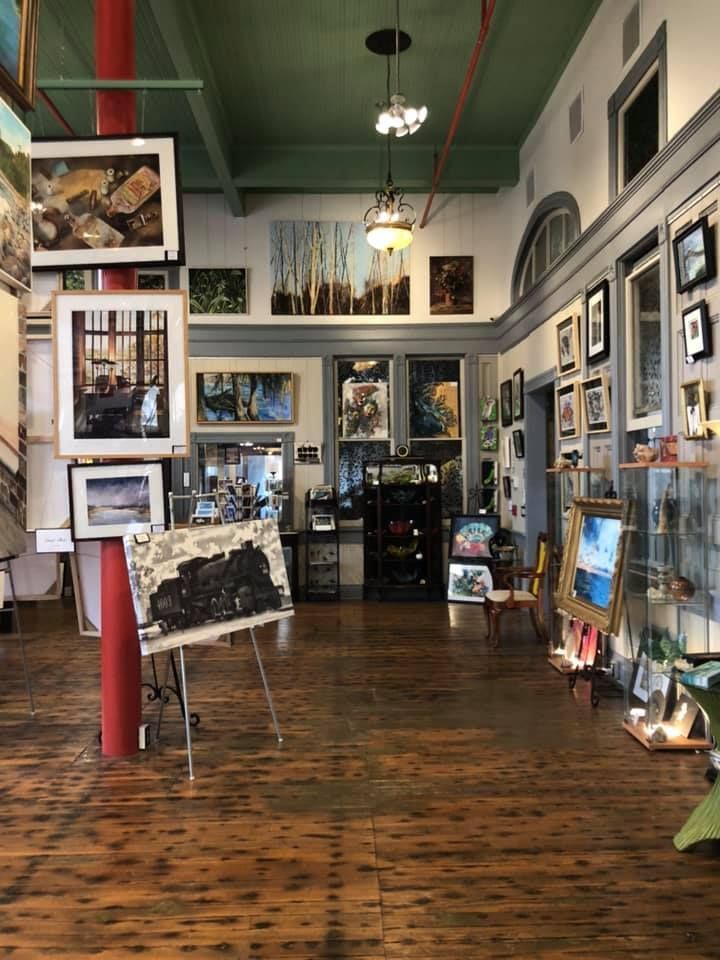 Art gallery interior with paintings on walls and floor, red pillar, wooden floor, and green ceiling.