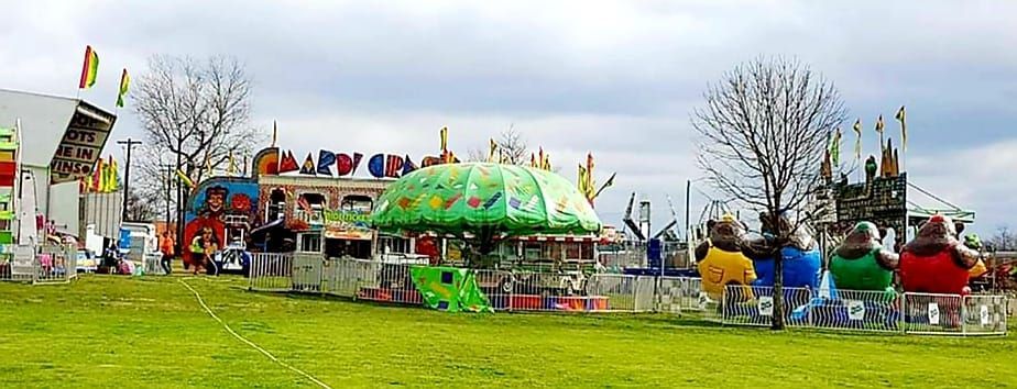 Carnival rides and games on a grassy field, under a cloudy sky.