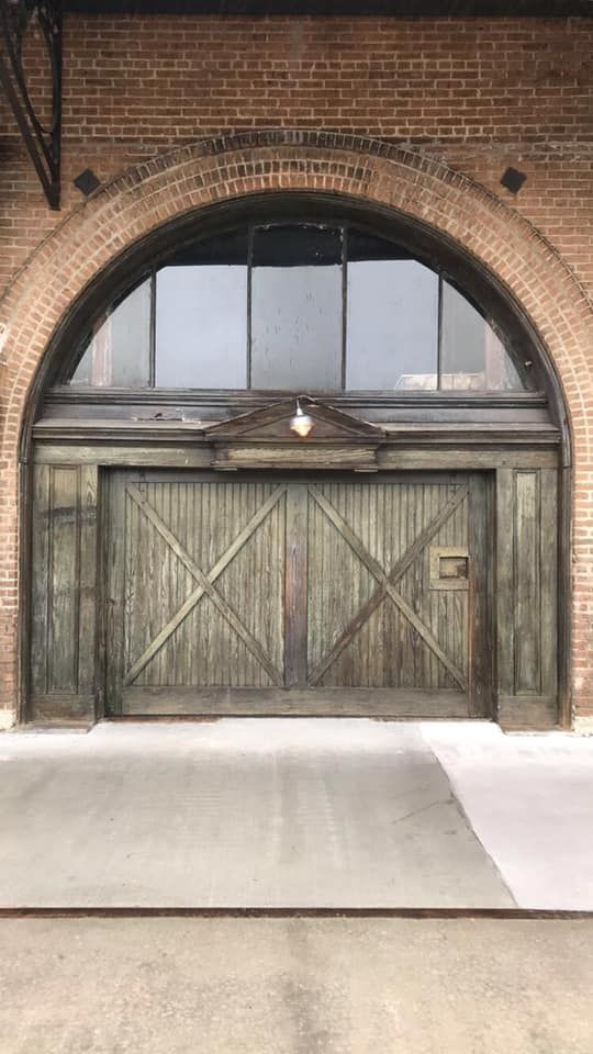 Weathered green wooden doors set in brick arched doorway; large window above.