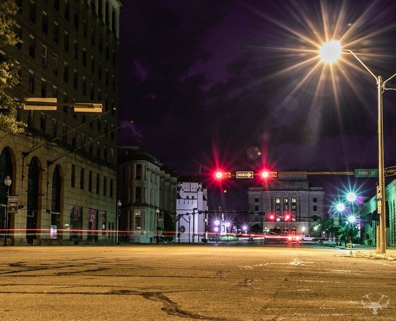 Nighttime city street scene with buildings, streetlights, and traffic lights.