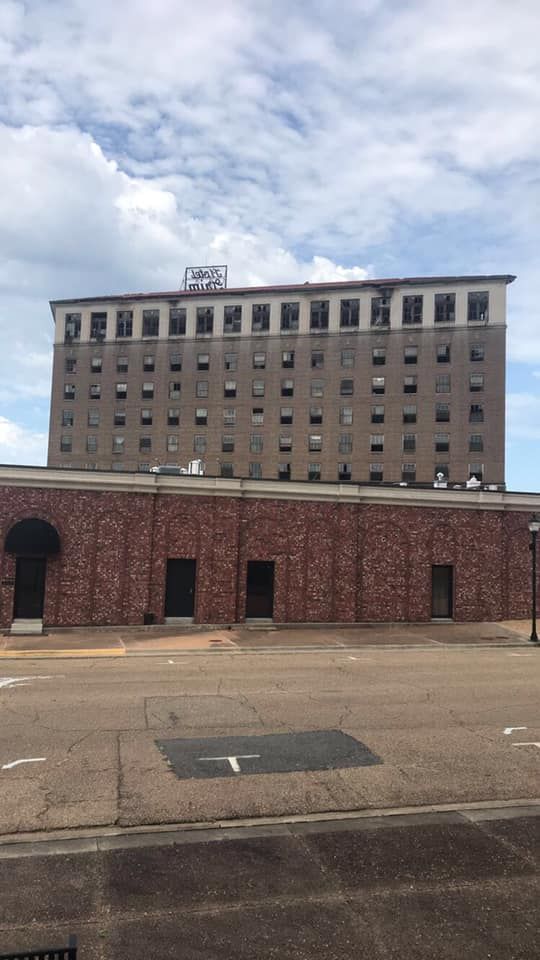 Tall, weathered building with many windows sits atop a brick structure against a cloudy sky.
