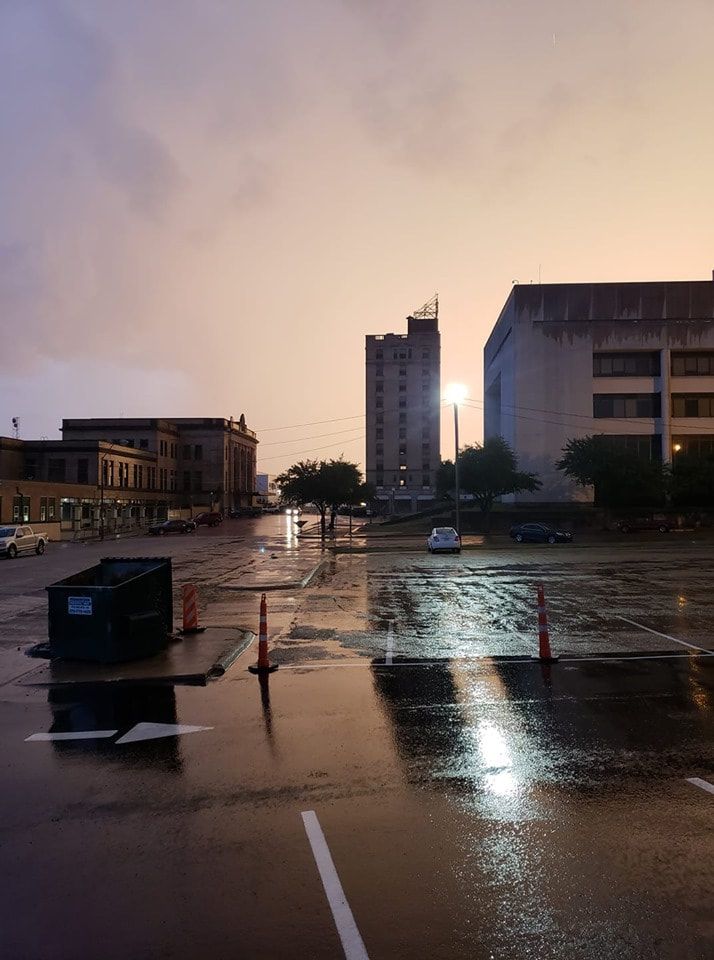 Wet city street after a rainstorm. Buildings line the street under a dusky pink and gray sky.