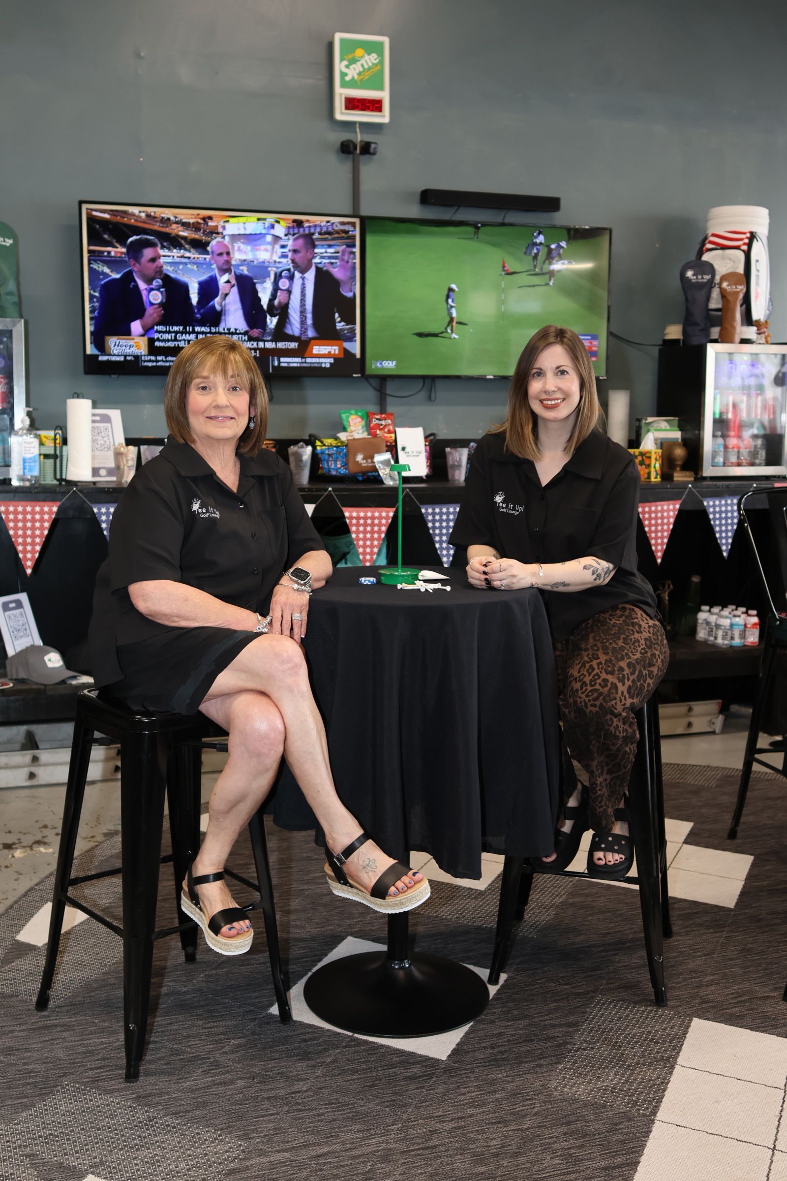 Two women seated at a small table in a sports bar with TVs showing a football game.
