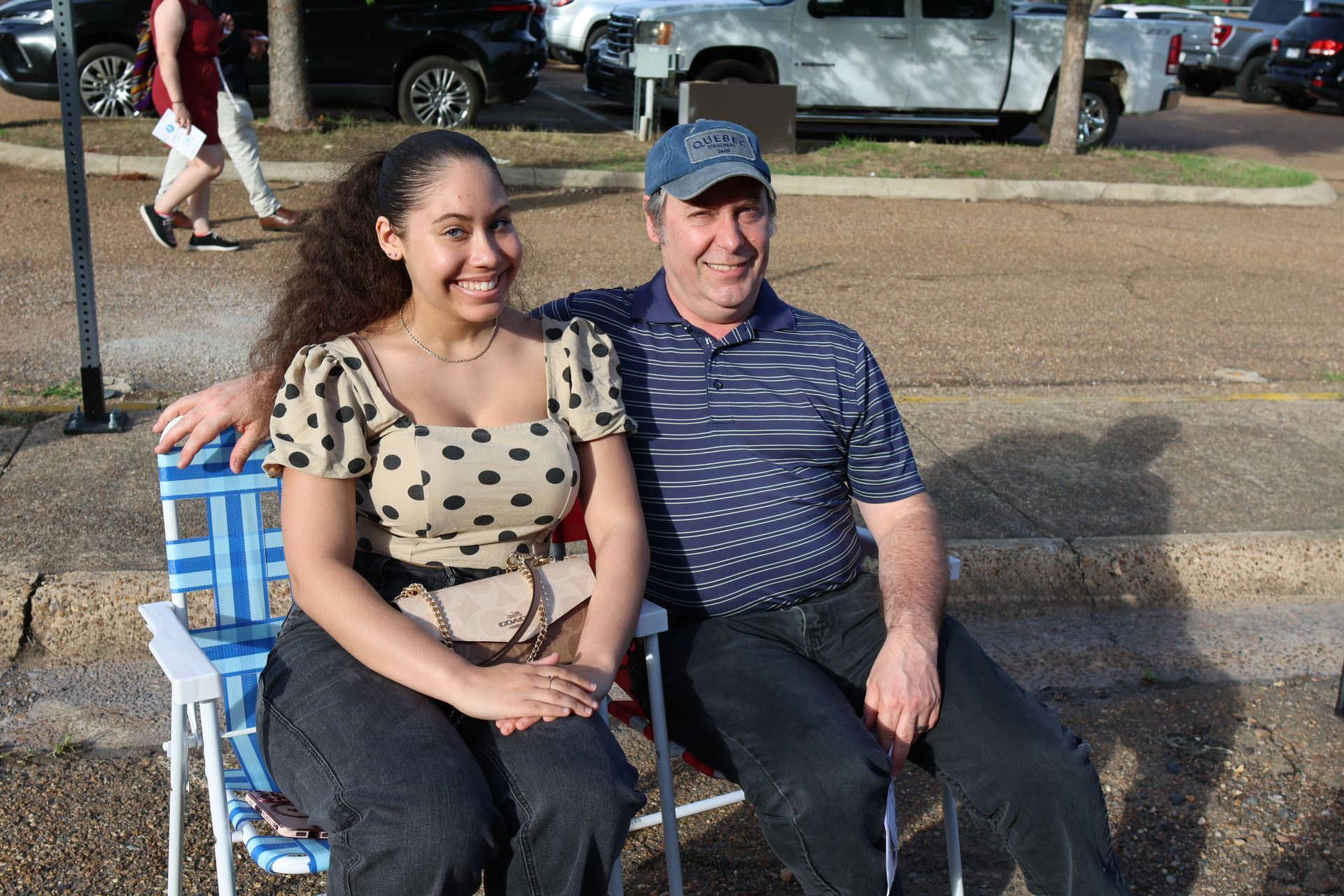 Two people seated outdoors on folding chairs, smiling in sunlight