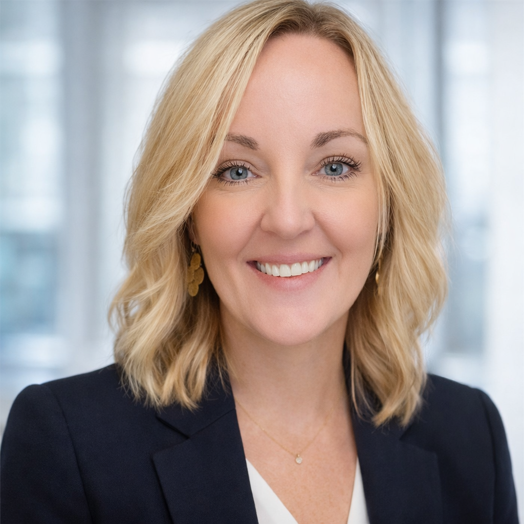 Smiling blonde professional in a dark blazer against a bright office background