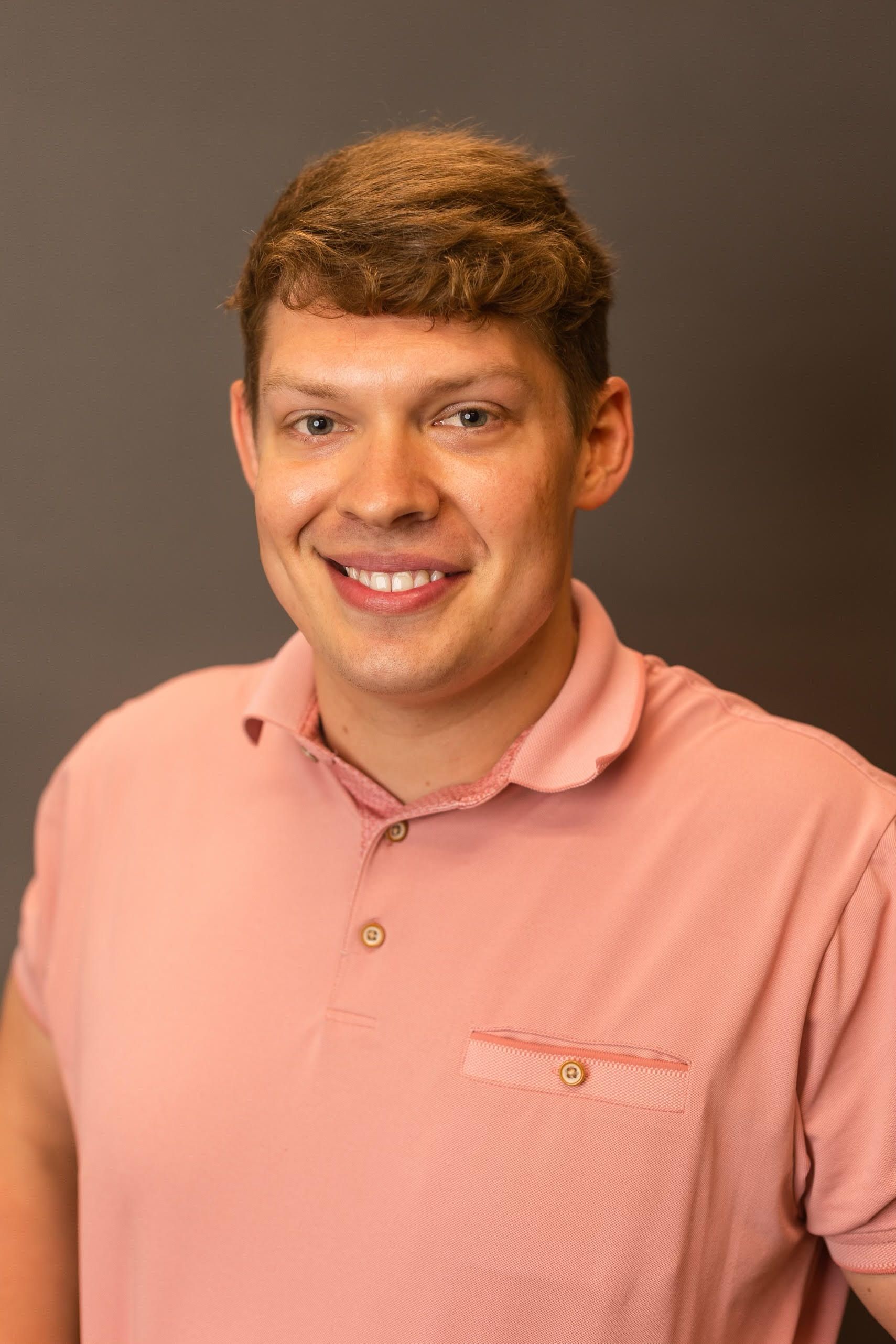 Smiling man in a pink polo shirt against a plain brown background