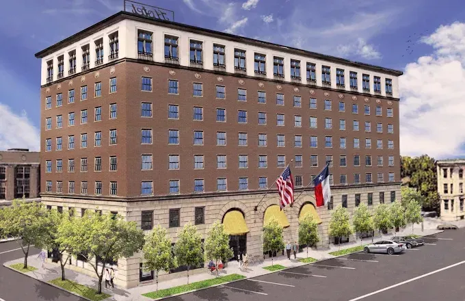 Hotel exterior with brick facade, flags, trees, and cars on street.