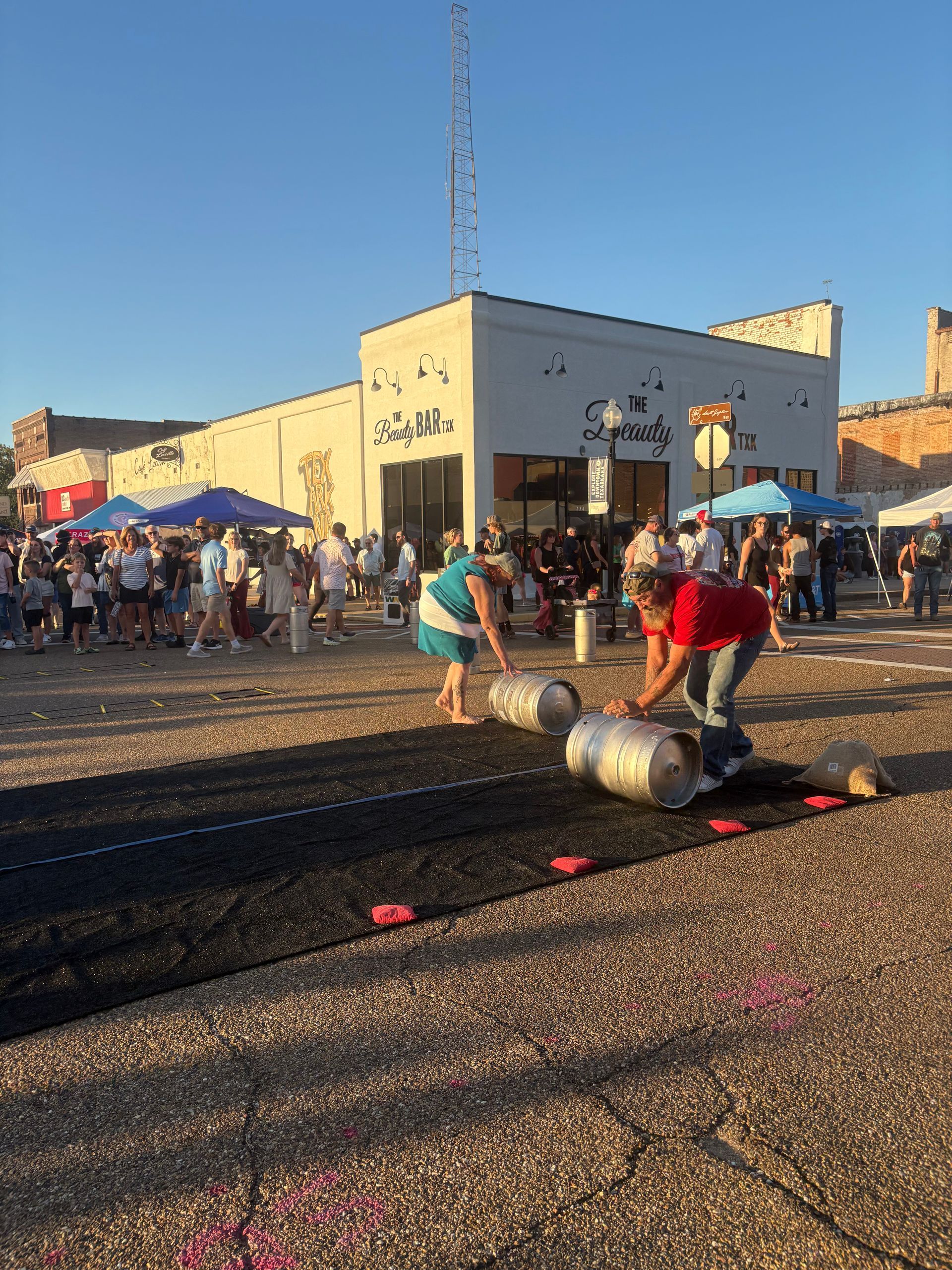 Two people rolling barrels on a black track in front of a building during an outdoor event.