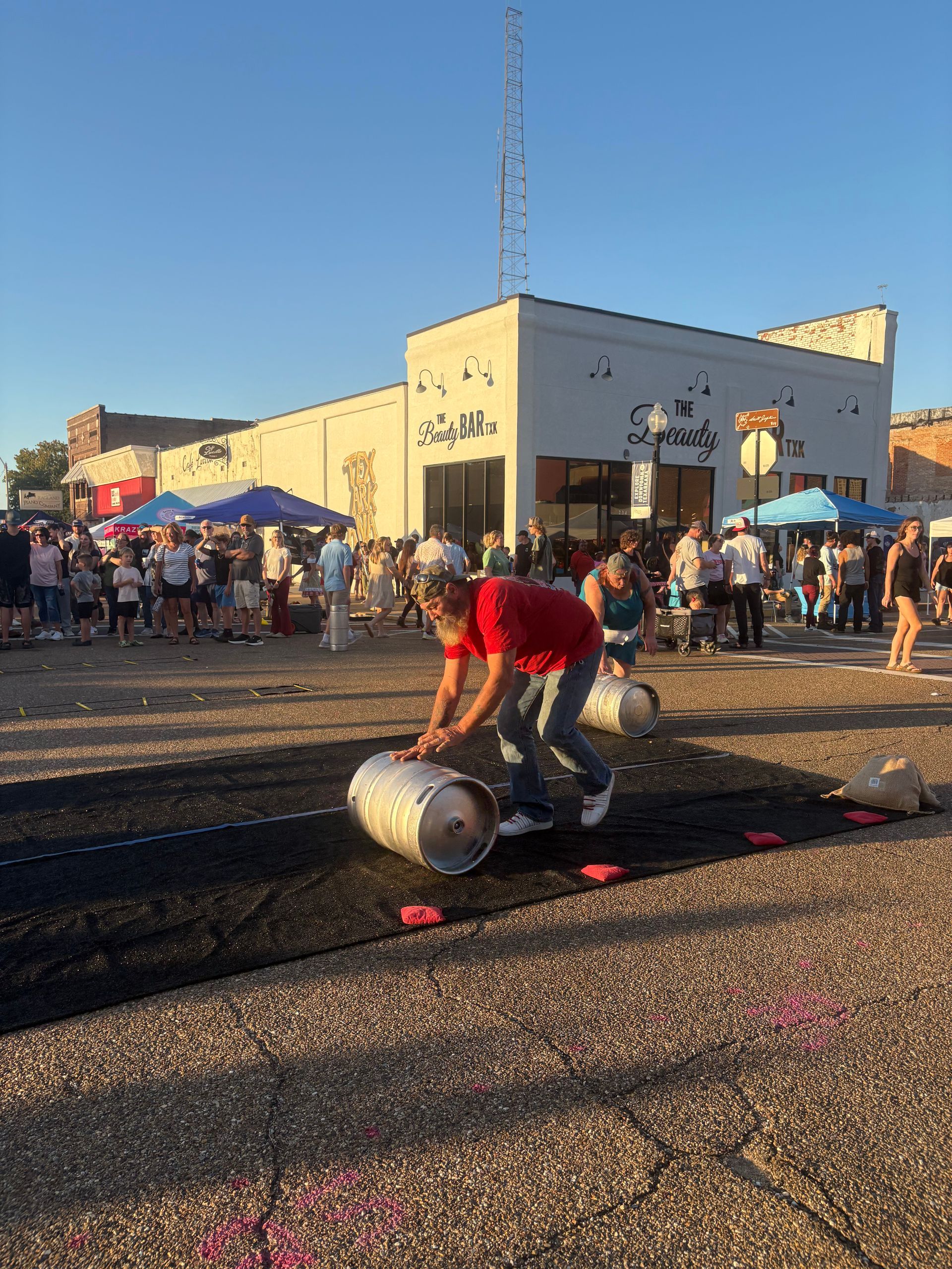 Man rolls a metal barrel on a dark surface, in front of a crowd gathered on a street.