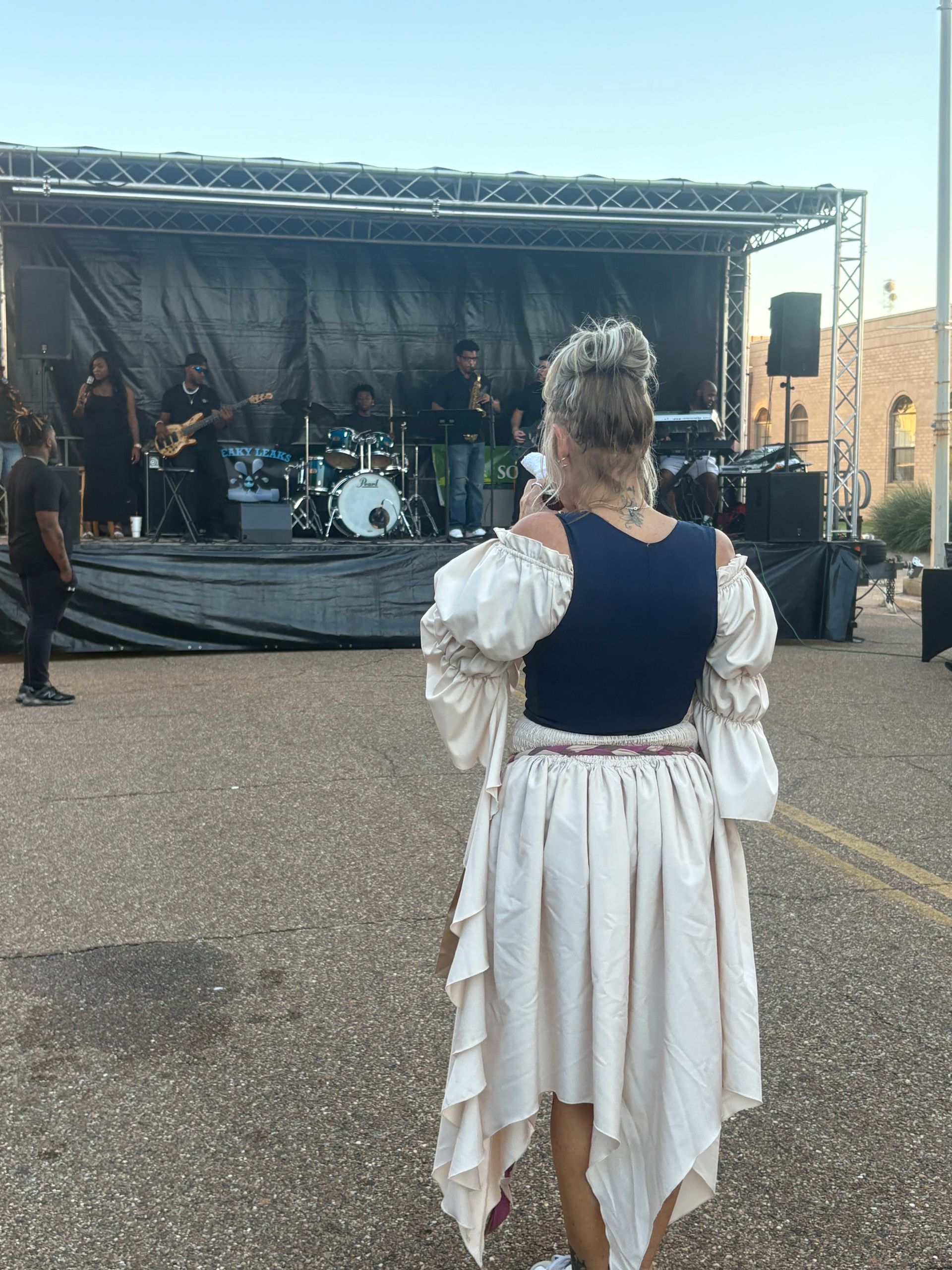 Woman in a dress facing stage with band performing outdoors.