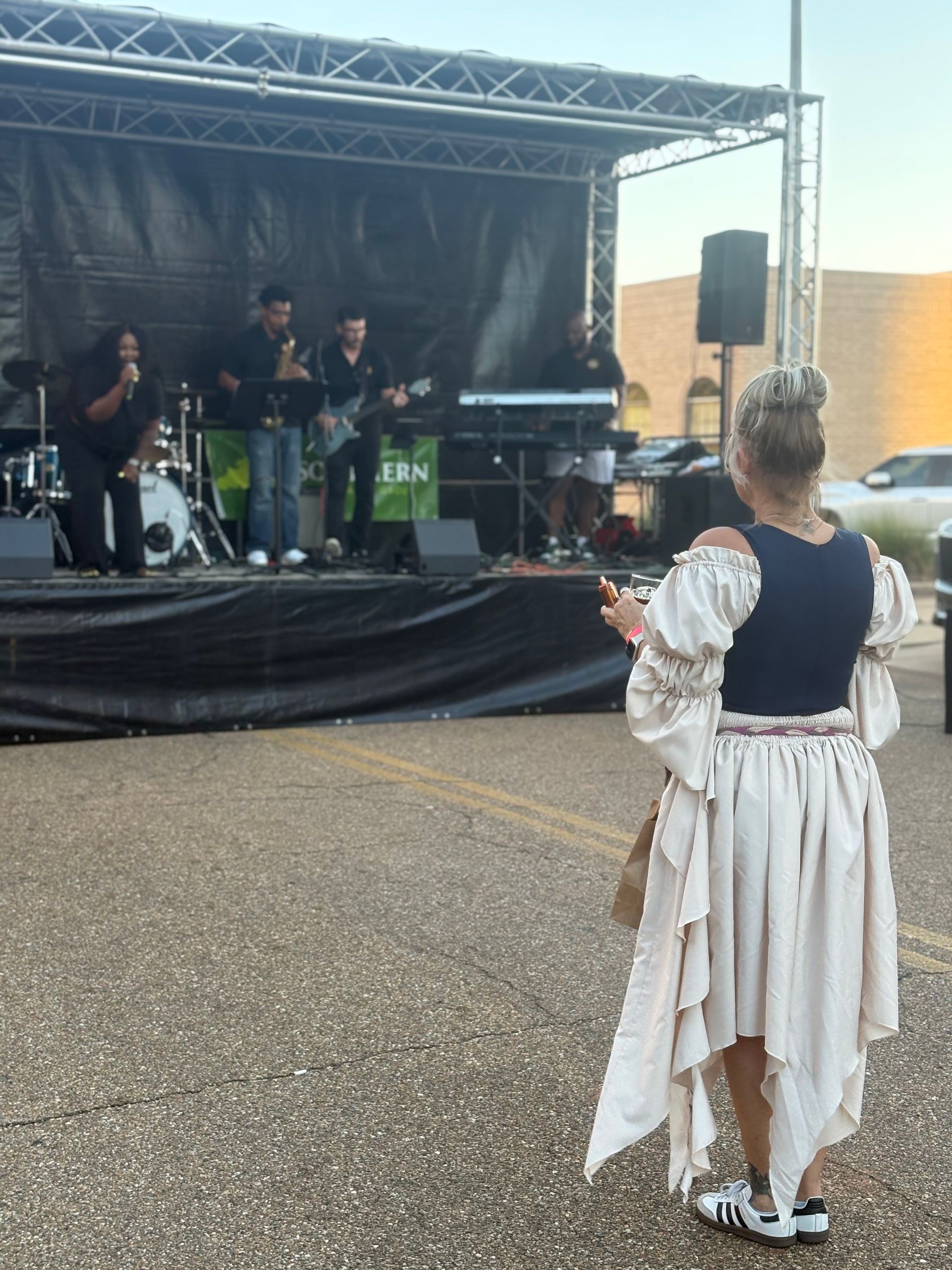 Woman in costume watches a band on an outdoor stage.