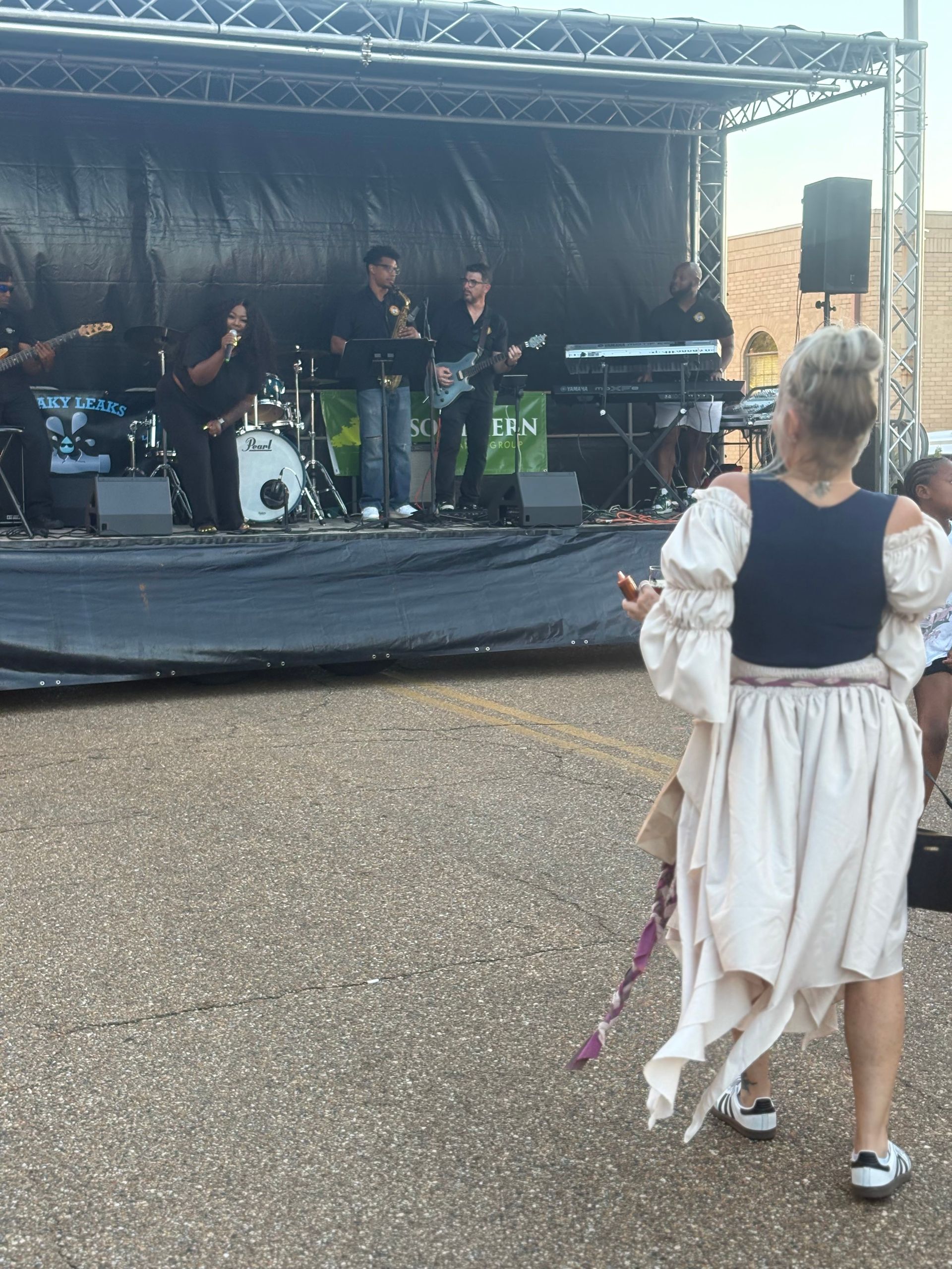 A band performs on a stage; a woman in a flowy dress dances in front.