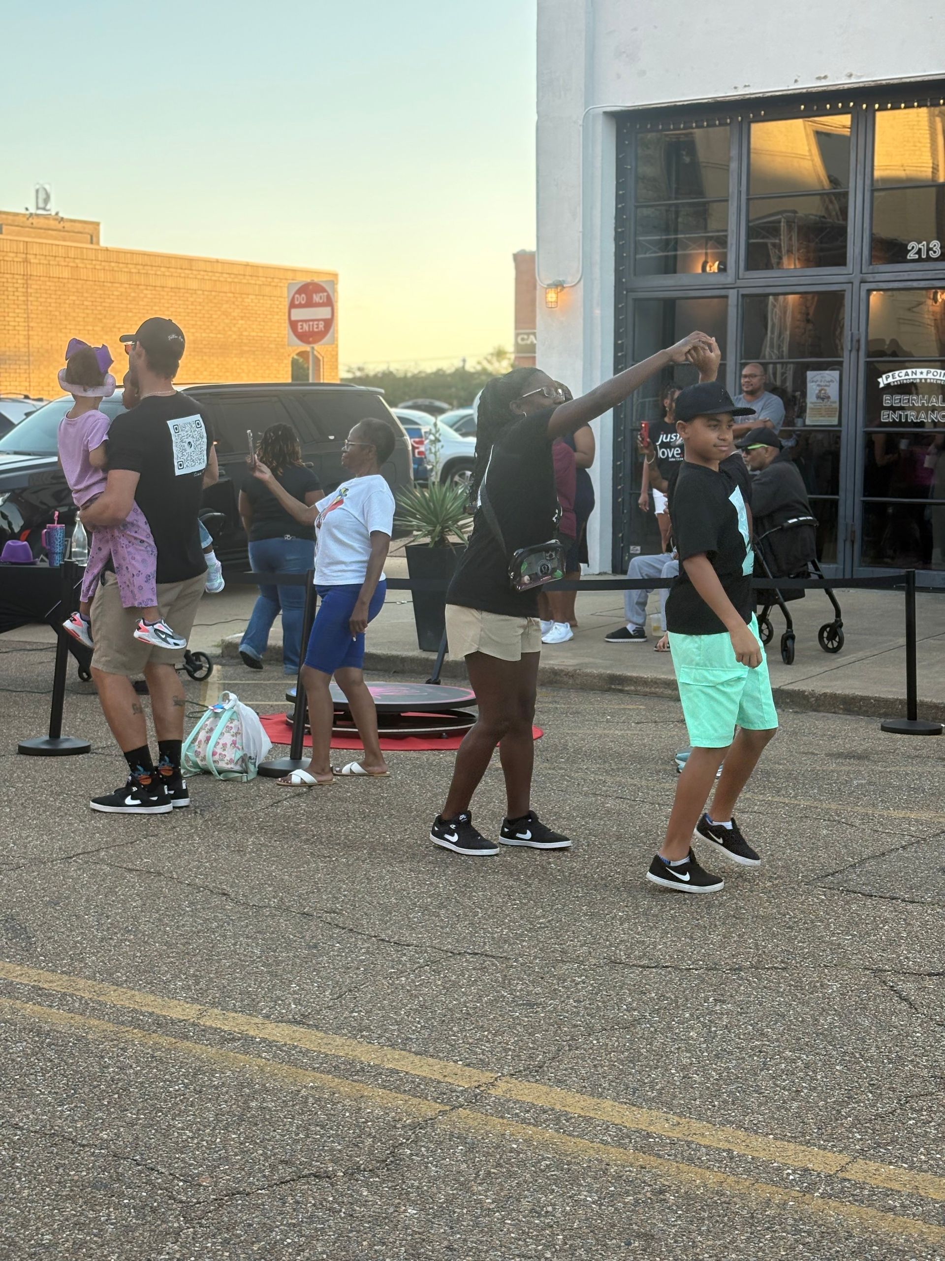 People dancing outside a building with glass doors, some wearing black shirts and shorts.