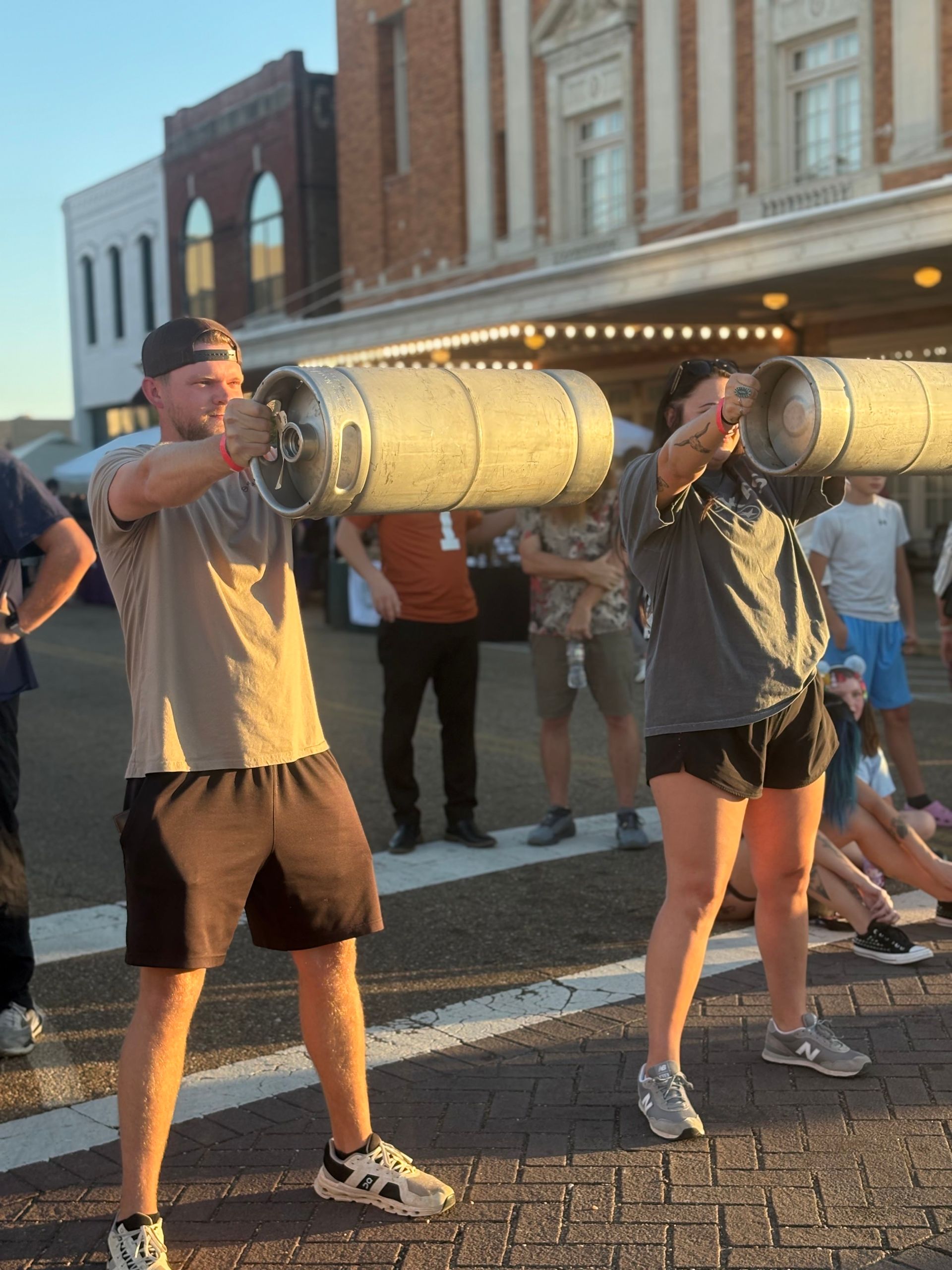 Two people holding a large, cylindrical object outdoors; downtown setting with other people.