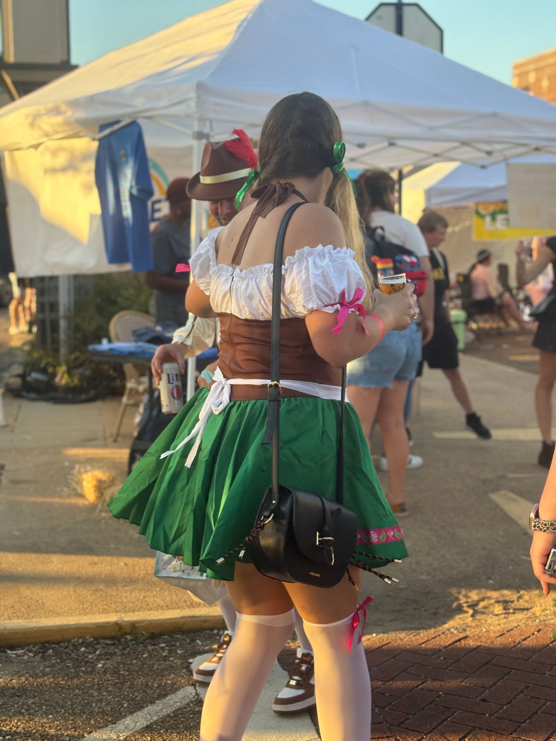 Woman in traditional German attire at an outdoor event, wearing a green skirt and holding a cup.