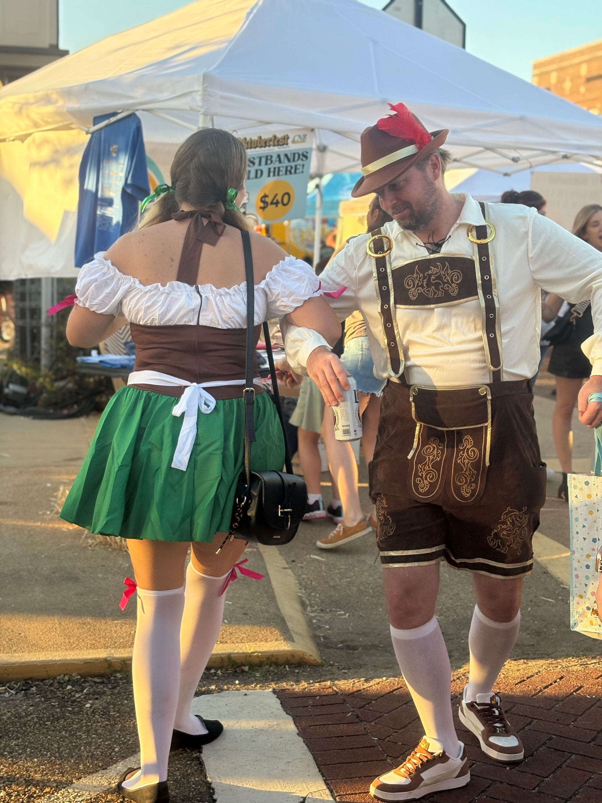 Two people in traditional German attire dance near a festival tent.