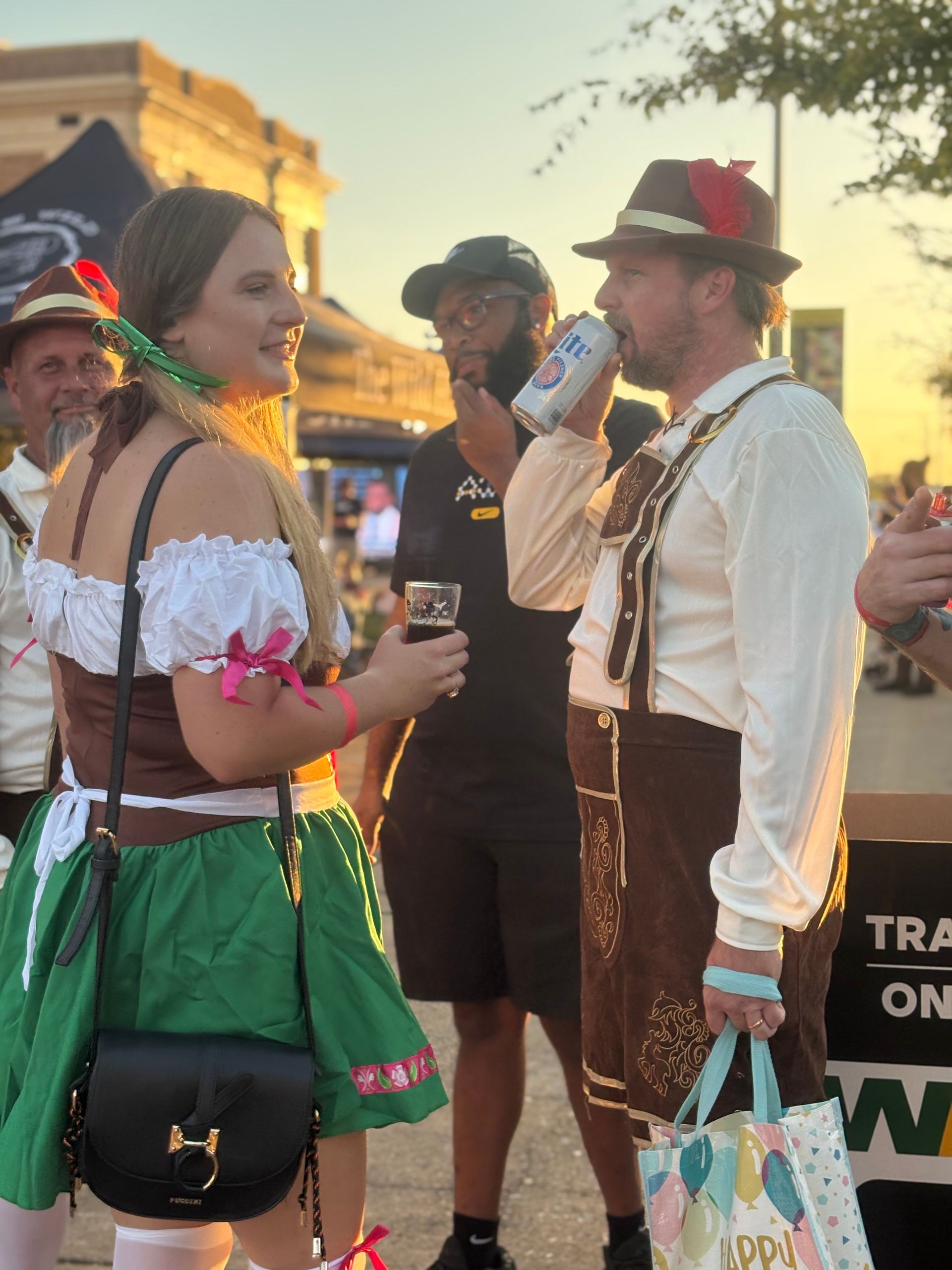 People in traditional German attire at an outdoor event, drinking beer.