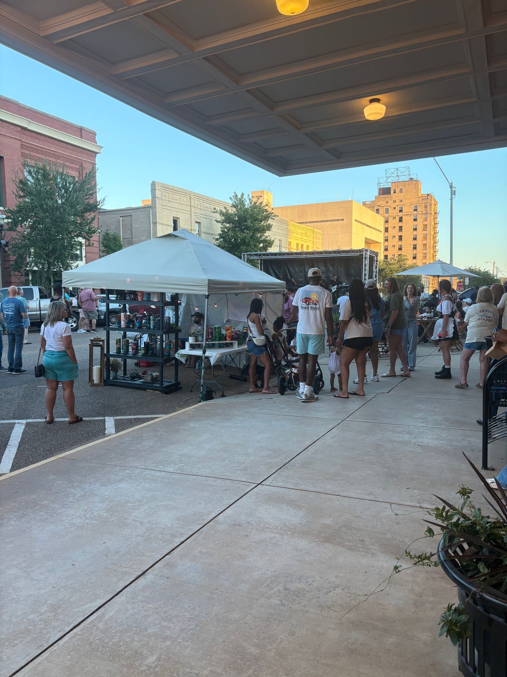People gather at an outdoor market under a covered area, with vendors and tents set up.