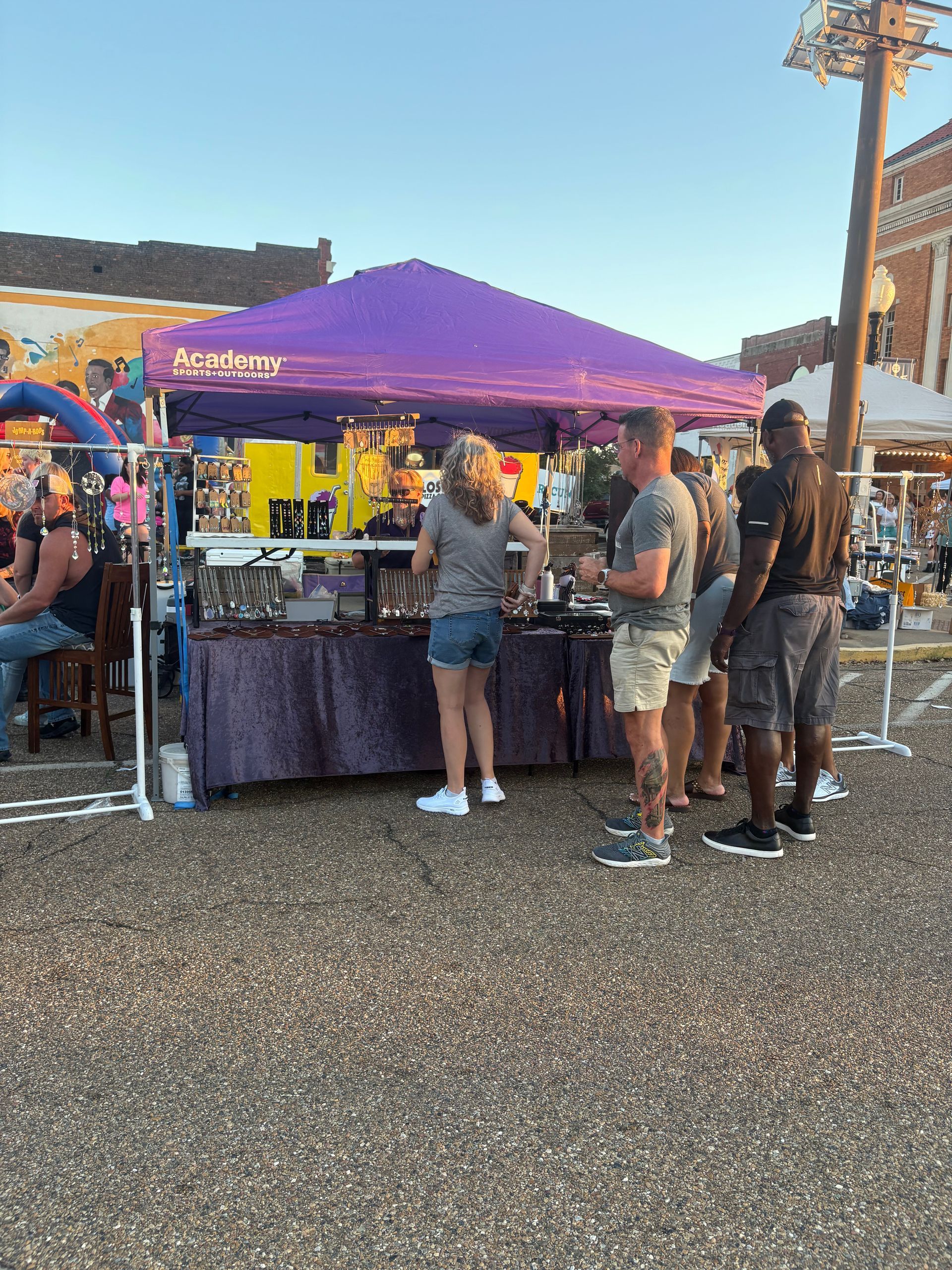 People looking at items displayed at a purple tent in a market setting.