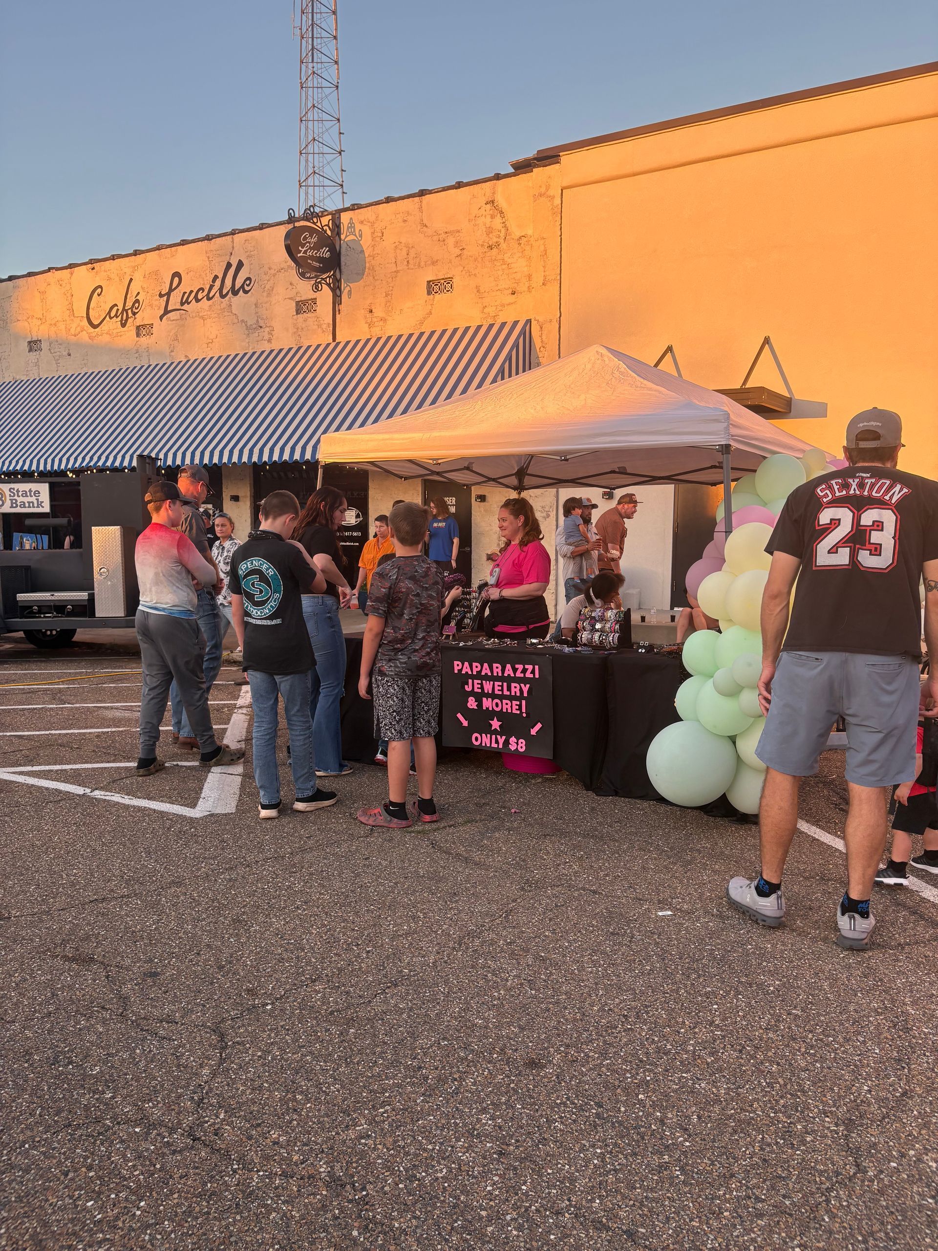 Outdoor market with a tent, merchandise, and people milling about. Building with 