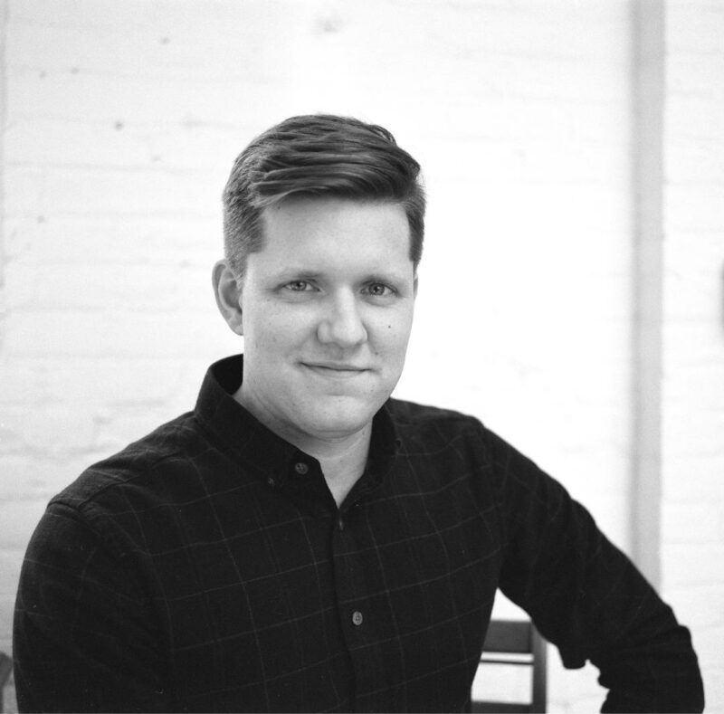 Portrait of a smiling person in a dark shirt against a light background
