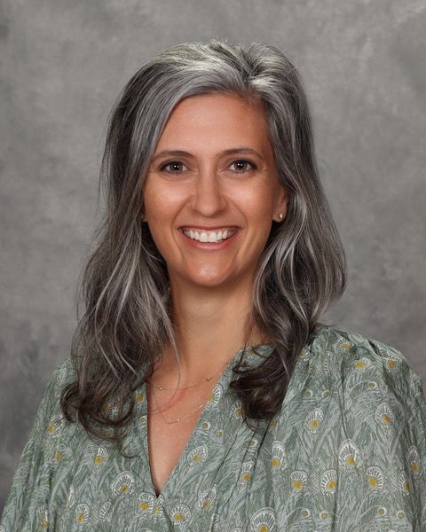 Portrait of a smiling woman with gray hair in a patterned blouse against a gray backdrop
