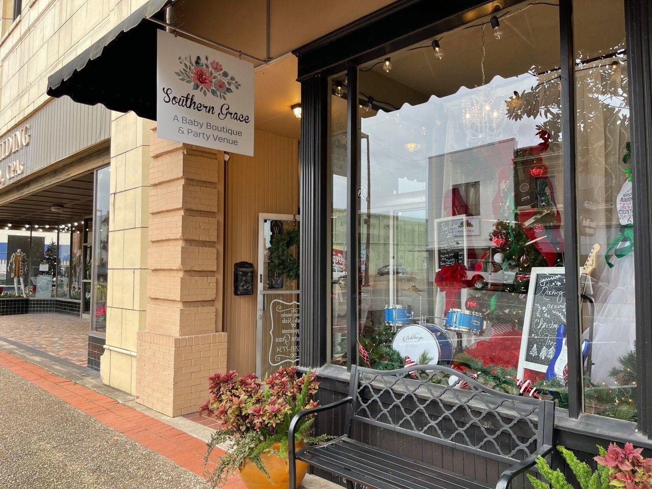 Storefront with large display windows, festive holiday decorations, and a hanging sign along a brick sidewalk