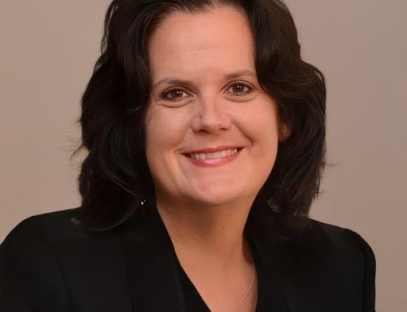 Smiling woman with dark hair in a black blazer against a neutral background
