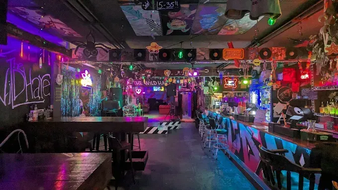 Interior of a brightly lit, alternative bar. Decorations and neon lights create a dark, colorful atmosphere.