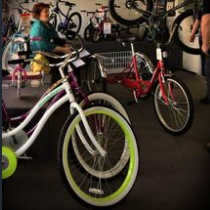 Bikes of various styles for sale in a shop. A woman sits nearby.