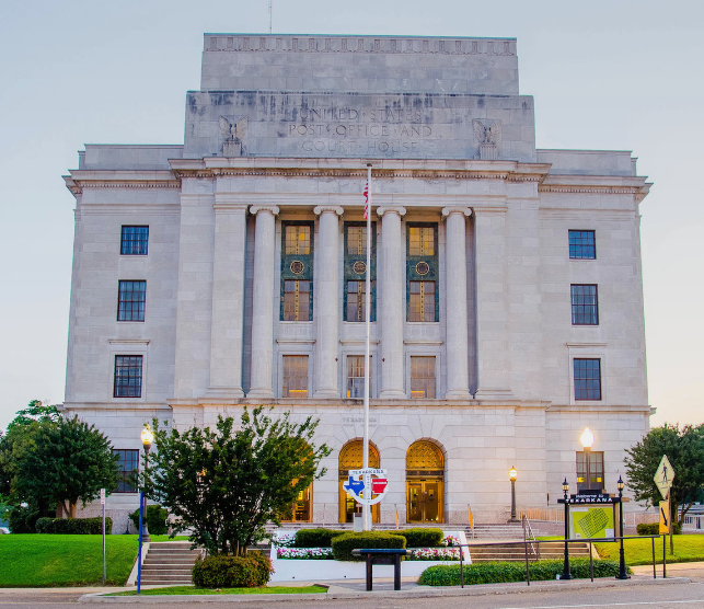 Beige courthouse with columns, flag, and green lawn.