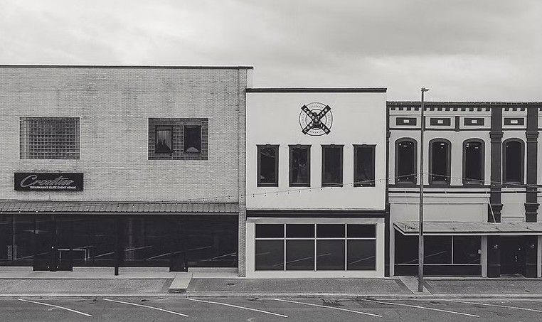 Black and white photo of three old brick storefronts under an overcast sky.
