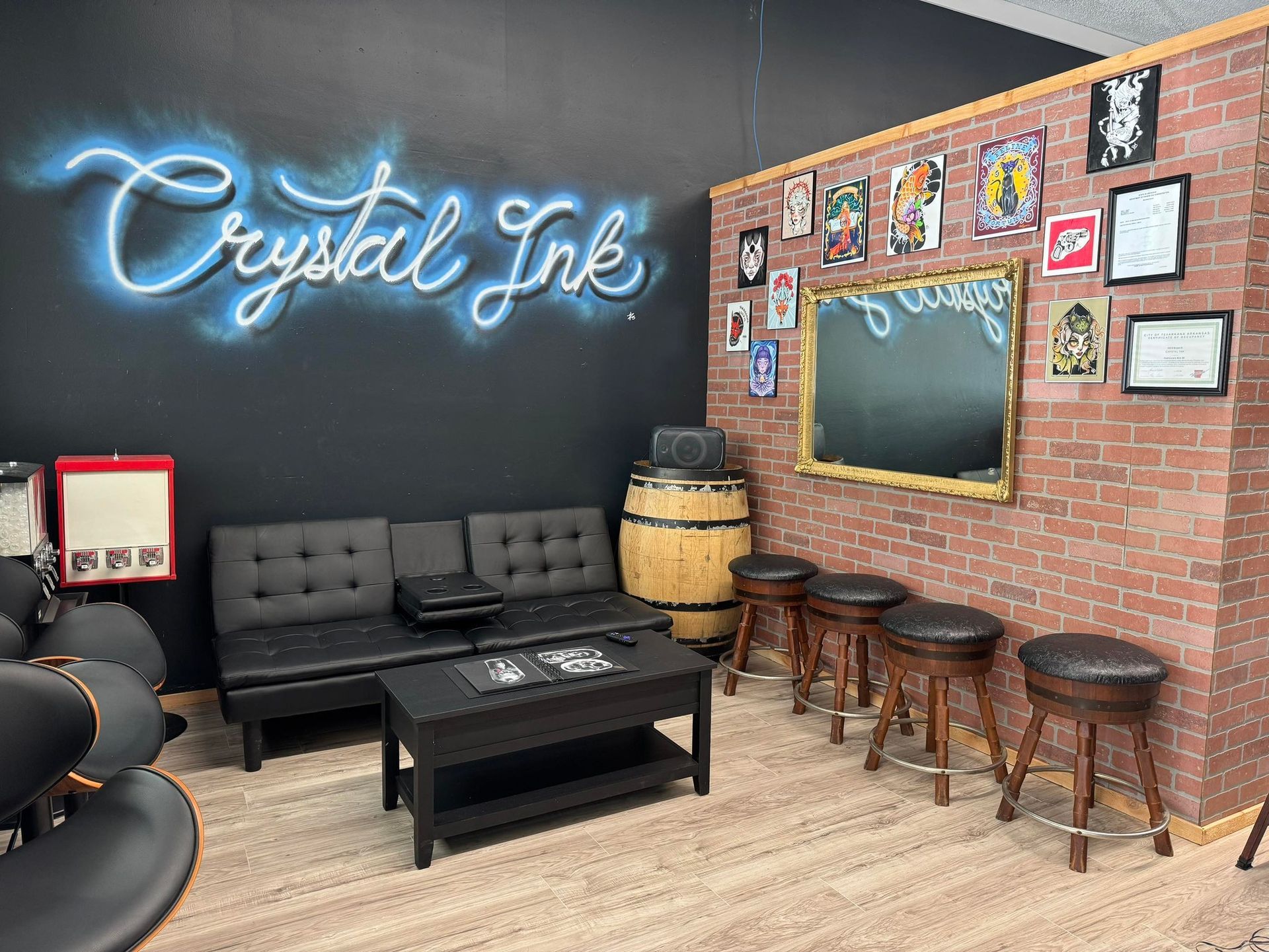Tattoo parlor interior: black walls, neon sign, brick accent, seating, posters, and stools.