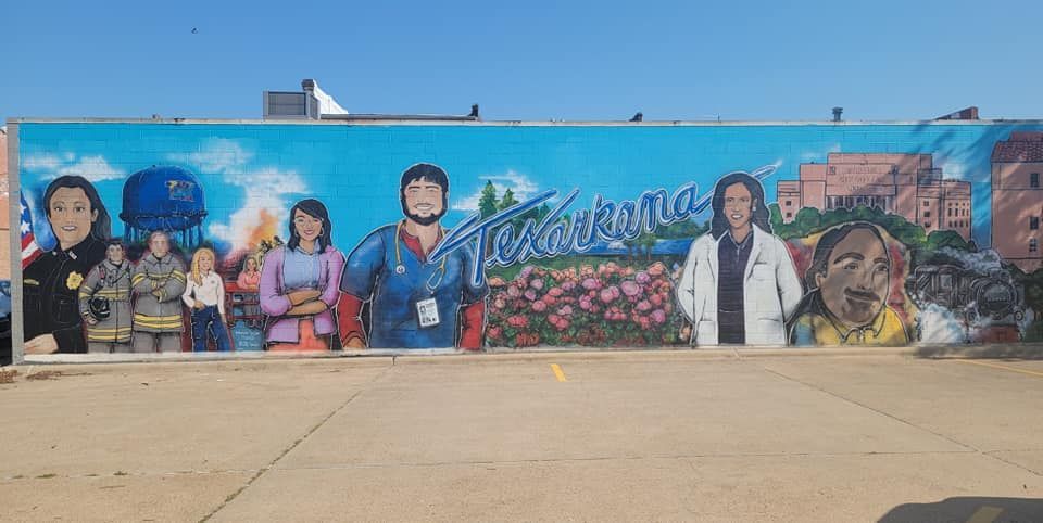 Mural featuring various community figures against a blue sky, including first responders, medical personnel, and a child.