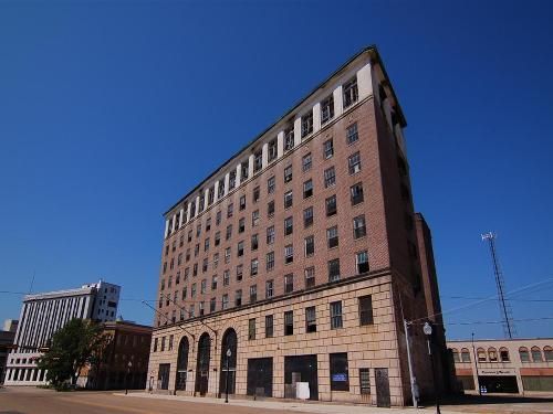Tall brick building under a clear blue sky. Street-level windows and arched entries.
